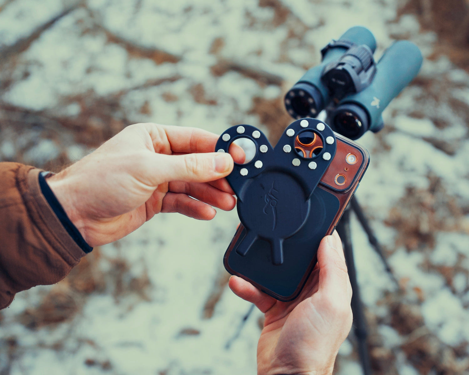 Person holding a device with a lens attachment in a snowy landscape